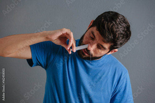 Nasal wash. Man flushng his nose with syringe and saline isolated on gray background