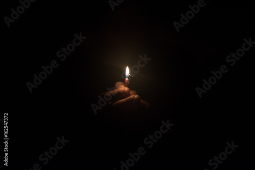 Hand holding burning candle in the dark