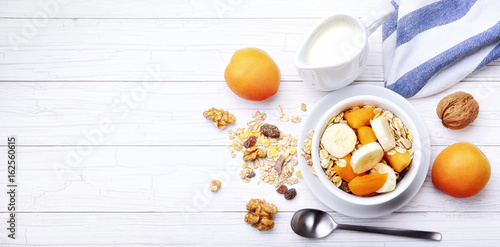 Breakfast, milk with muesli and fruit: apricots, banana and walnuts
