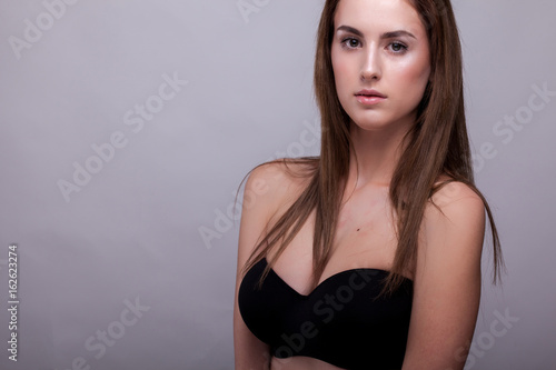 Sexy woman in bra with natural make up on gray background in studio photo. Beauty and fashion.