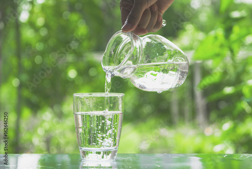 Female hand pouring water from pitcher to glass on nature background