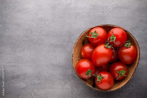Small plum tomatoes in a wooden bowl on a gray background.