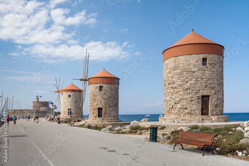 Windmill Papagiorg whit Vati in Rhodes harbor. Old defensive stands and windmills. Wharf harbors, boats and sailing ships. Historic pier and beach.