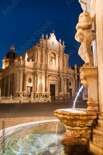 Night view of the fountain at the basis of famous lava stone elephant in the main square of Catania, Sicily, with a view of St. Agatha church