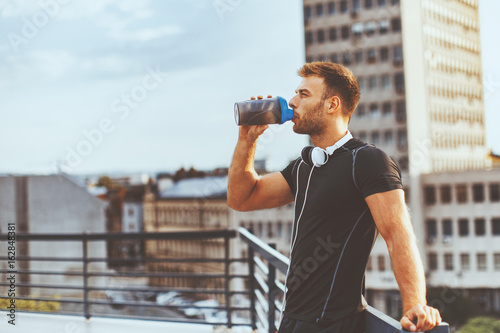 Young man resting on the roof of the building after workout and drink water