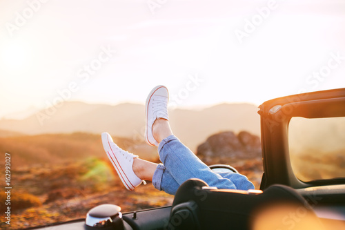 Happy woman rests and pushes her shoes out of the convertible to enjoy the view