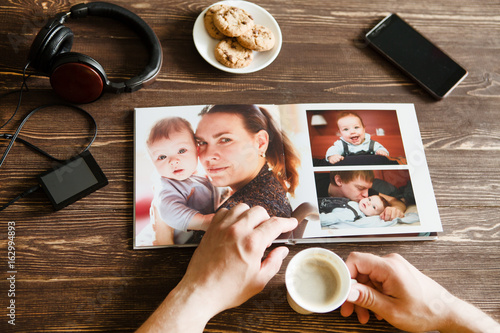 the Hand man holding a family photo album against the background of the a wooden table 