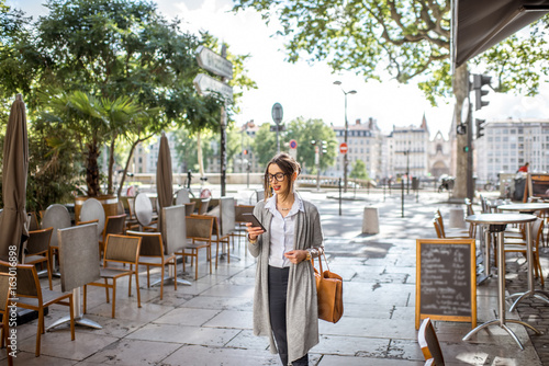 Young stylish businesswoman walking with phone and bag on the street with cafes in Lyon old town