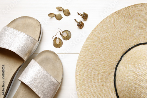 golden earrings, straw hat, slippers- summer accessories on wooden background