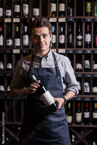 Portrait of a sommelier standing in a wine cellar holding a glass of wine and showing thumb up, during a degustation