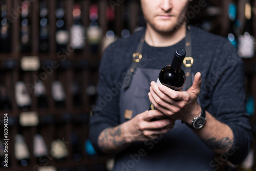 Focused young male sommelier in suite looking at red wine in bottle