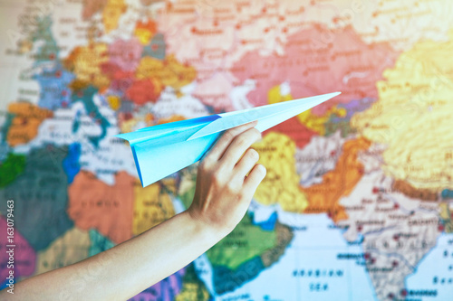 hand with paper origami airplane on world map background