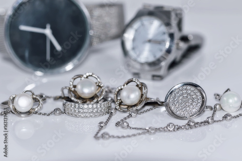 Silver earrings with pearl on the background of watches