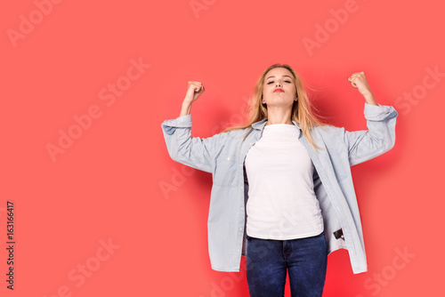Young blonde girl shows her strength on red background