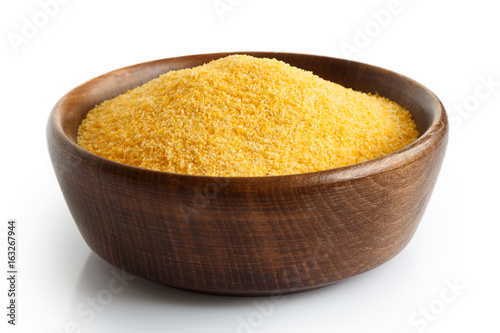 Uncooked cornmeal in dark wooden bowl isolated on white.