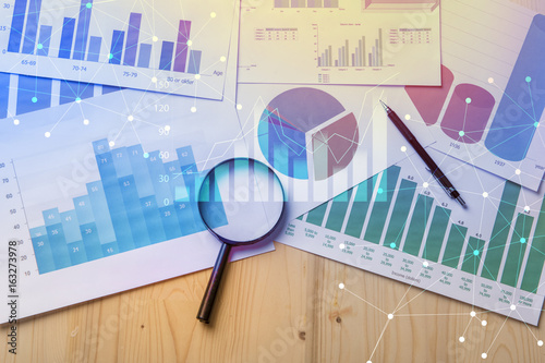 Magnifying glass and documents with analytics data lying on table,selective focus