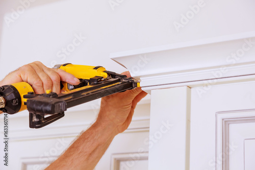 Carpenter brad using nail gun to Crown Moulding on kitchen cabinets framing trim,