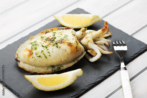 Close-up of cuttlefish with garlic and parsley and lemon on whiteboard.