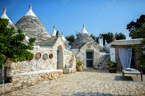 Typical trulli buildings with conical roofs, among green plants and flowers, main touristic district, Val d' Itria, Apulia region, Southern Italy,