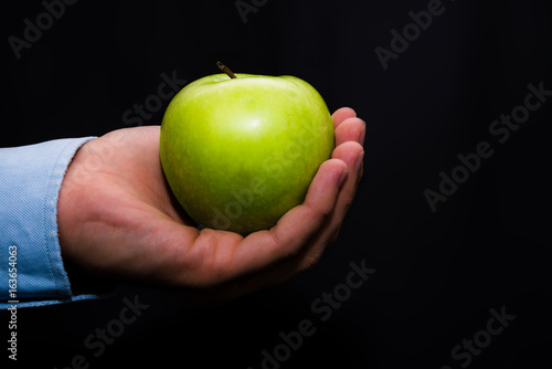 Zielone jabłko trzymane w ręce na ciemne czarne tło