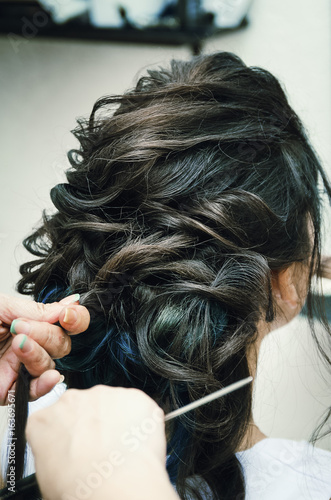 Closeup of a professional hairdresser's hands doing a hairstyle in a beauty salon. Model brunette, in the hair some of the strands are painted blue. The concept of fashionable stylish hairstyle.