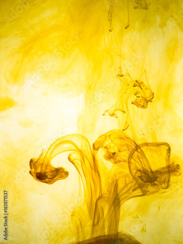 Ink swirl in a water on yellow background. The paint splash in the water. Soft dissemination a droplets of colored ink in water close-up. Abstract background. Explosion of color splashes acrylic ink.