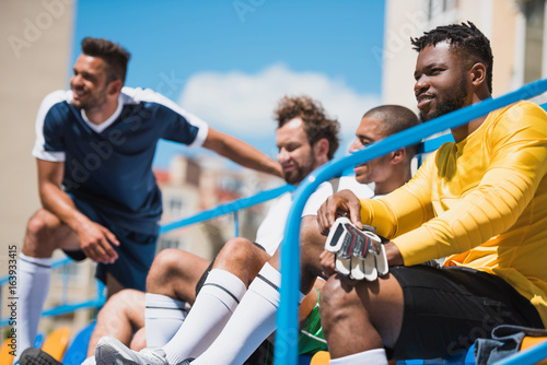 multicultural soccer team sitting on stadium during soccer match