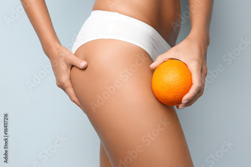 Young woman holding orange on light background. Cellulite problem concept