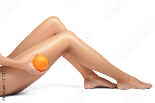 Female legs and orange on white background. Cellulite problem concept