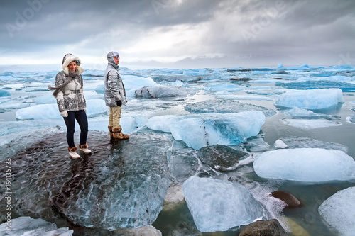 Extremely beautiful tourists stand on the massive icebergs in lake Jokulsarlon in Iceland in winter