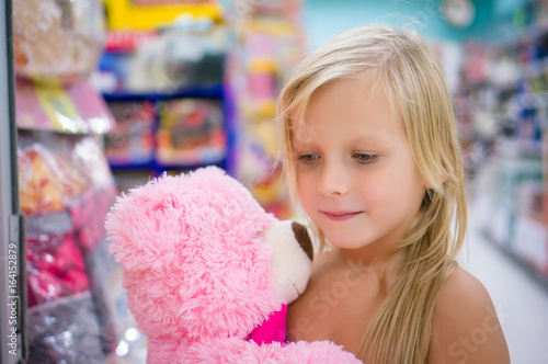 Adorable girl with pink plush teddy bear in shop