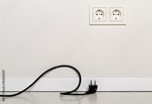 Black power cord cable unplugged with european wall outlet on white plaster wall