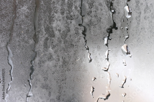 Detailed texture of water dripping down glass in a humid room.