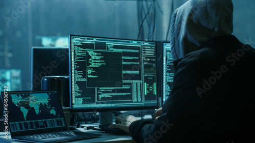 Dangerous Hooded Hacker Breaks into Government Data Servers and Infects Their System with a Virus. His Hideout Place has Dark Atmosphere, Multiple Displays, Cables Everywhere.