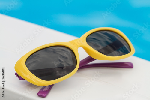 Children sunglasses lying on a deck-chair on blue water background