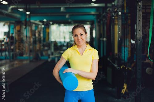 Girl in fitness club. Young female athlete with a Mat for stretching in the hands, ready to workout