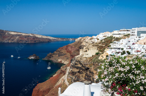 Oia Village, Santorini Cyclade islands, Greece. Beautiful view of the town with white buildings blue church's roofs and many coloured flowers.