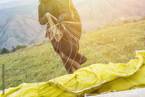 Close up of a paraglider on a mountain top packing his parachute. Flying over a mountain valley in summer sunny day. Extreme sport.