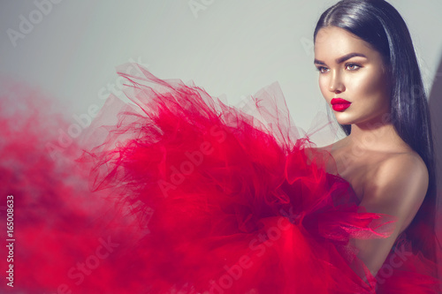 Gorgeous brunette model woman in red dress posing in studio