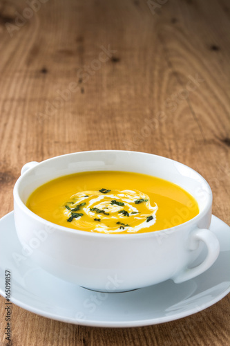 Pumpkin soup in white bowl on wooden table 
