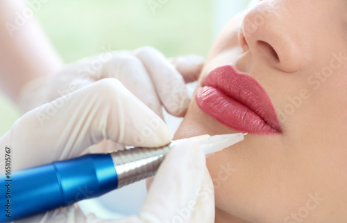 Young woman having permanent makeup on lips in beautician salon