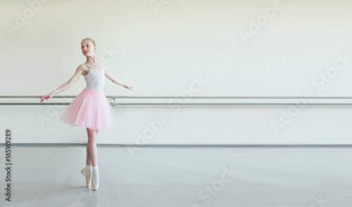 Cute little ballerina in pink ballet costume and pointe shoes is dancing in the room. Kid in dance class. Child girl is studying ballet. Copy space.