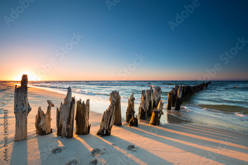 Zachód słońca na plaży nad Morzem Bałtyckim i stary drewniany falochron