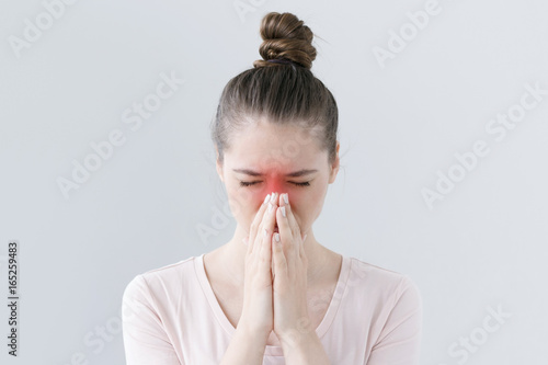Closeup of young European female isolated on gray background looking stressed, putting hands together as if she is praying with closed eyes to overcome depression and find solution to problem.
