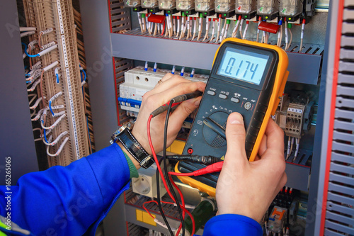 Electrical Engineer adjusts electrical equipment with a multimeter in his hand closeup.