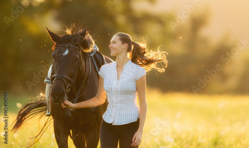 Young woman running with her horse in evening sunset light