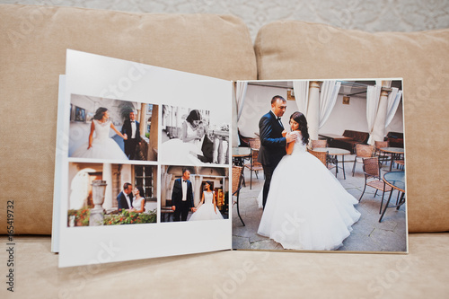 Pages of wedding photobook or wedding album on the sofa with cushions on the background.