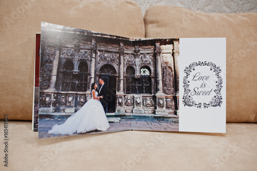 Pages of wedding photobook or wedding album on the sofa with cushions on the background.