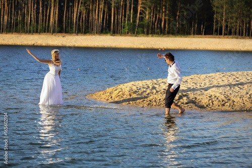 Młodzi ludzie chlapią się wodą na brzegu jeziora, ślub, wesele.