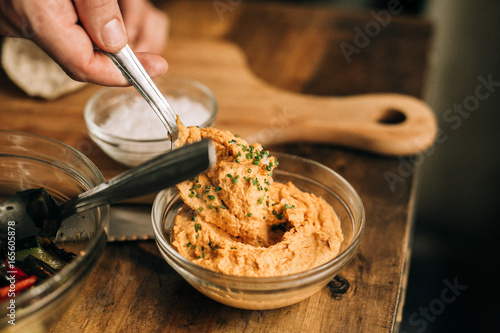 Person takes some hummus out of bowl, served with fresh garbanzo beans, mediterranean herbs, extra virgin olive oil, ready for dip or spread on bread or pita